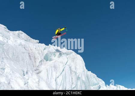 Ein springender Skifahrer, der von einem Gletscher gegen einen blauen Himmel hoch in den Bergen springt. Professionelles Skifahren Stockfoto