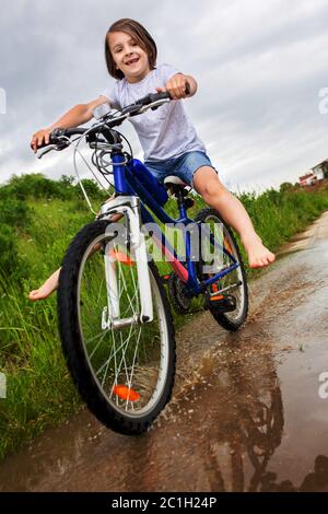 Kind, Junge, Fahrrad fahren in schlammiger Pfütze, Sommerzeit an einem regnerischen Tag Stockfoto