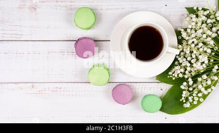 Bunte Makronen, eine Tasse Kaffee und Lilien des Tals auf Holzhintergrund, Nahaufnahme flach lag. Konzept von Frühstück und Frühlingszeit. Kopierbereich Stockfoto