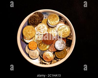 Kleine Geldmünzen in einem Teller auf schwarzem Hintergrund. Stockfoto