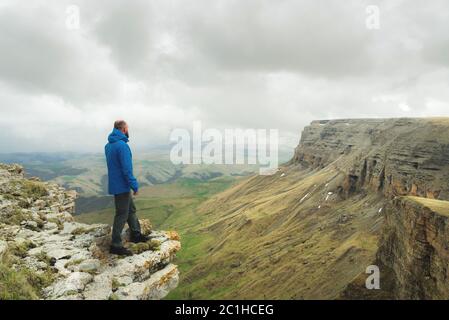 Bärtiger Hipster-Tourist, der am Rande eines Felsens steht und auf einem epischen Plateau in die Ferne blickt. Das Konzept von Stockfoto