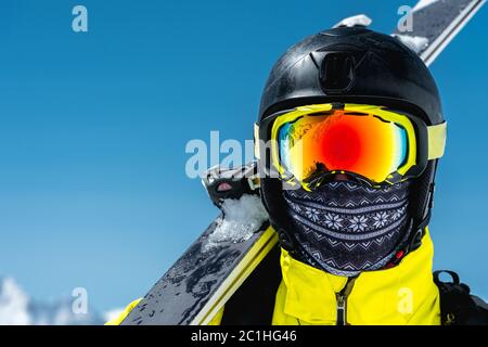 Ein großes Porträt eines Skifahrers in Schutzhelm und Brille - eine Maske und ein Schal neben den Skiern gegen die schneebedeckte mou Stockfoto