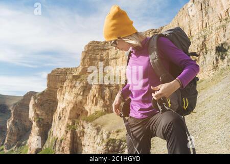 Mädchen Tourist in Sonnenbrille setzt einen Rucksack auf die Natur auf einem Hintergrund von epischen Felsen Vorbereitung für Trekking mit Klettern Stockfoto