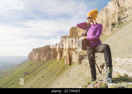 Mädchen Tourist in Sonnenbrille setzt einen Rucksack auf die Natur auf einem Hintergrund von epischen Felsen Vorbereitung für Trekking mit Klettern Stockfoto