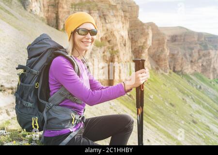 Lächelndes Mädchen Reisenden in einem gelben Hut und eine Sonnenbrille am Fuße der epischen Felsen mit einem Rucksack als nächstes und sieht Stockfoto