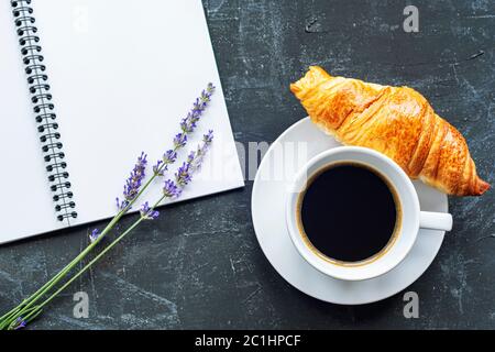 Tasse Kaffee mit Croissant, Notizblock und Lavendelblüten auf schwarzem Hintergrund, Draufsicht, flach liegend, Kopierraum Stockfoto