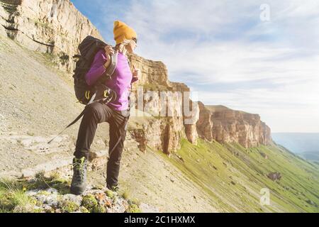 Mädchen Tourist in Sonnenbrille setzt einen Rucksack auf die Natur auf einem Hintergrund von epischen Felsen Vorbereitung für Trekking mit Klettern Stockfoto