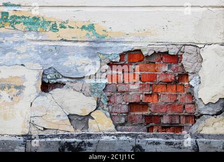 Eine alte Wand mit abblätterndem beigefarbenem Putz, unter dem rote Ziegelsteine zu sehen sind Stockfoto