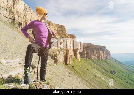 Mädchen Tourist in Sonnenbrille setzt einen Rucksack auf die Natur auf einem Hintergrund von epischen Felsen Vorbereitung für Trekking mit Klettern Stockfoto