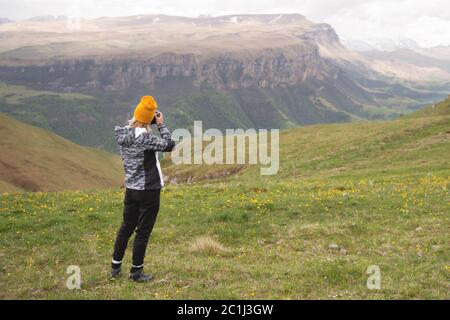 Ein junges Mädchen fotografiert an einem bewölkten Tag ein Plateau auf einem hohen Berg. Blick auf das Mädchen dahinter Stockfoto