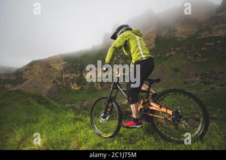 Ein Mann in einem Berghelm mit dem Mountainbike fährt um die schöne Natur bei bewölktem Wetter. Bergab Stockfoto