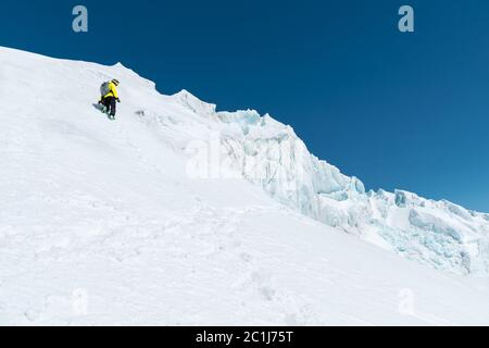 Ein Skifahrer in Helm und Maske mit Rucksack steigt auf einer Piste vor dem Hintergrund von Schnee und einem Gletscher. Backcountry Freeride Stockfoto