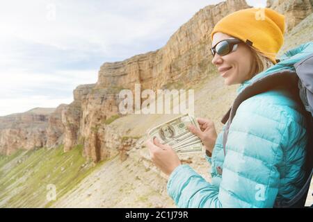 Ein Reisender in einem Hut und Sonnenbrille hält hundert Dollar Scheine in den Händen eines Fans vor dem Hintergrund von Felsen auf dem Nat Stockfoto