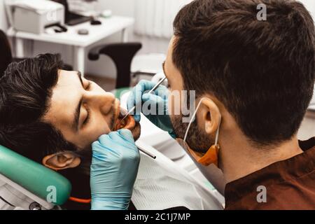 Ein junger Zahnarzt behandelt einen Patienten. Medizinische Manipulationen in der Zahnmedizin, Chirurgie. Professionelle Uniform und Ausrüstung eines Zahnarztes. Gesundheitswesen Stockfoto