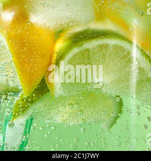 Ein natürlicher Fruchthintergrund mit Makrolimchen, Zitrone und einem farbigen Trinkhalm aus Kunststoff in einem Glasgefäß mit belüfttem Gasten Stockfoto