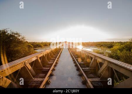 Alte Eisenbahnbrücke aus Stahl auf dem Fluss mit schönen Sonnenuntergang Stockfoto