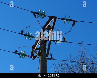 Stromleitungen über Kopf mit blauen Glasisolatoren und einem klaren blauen Himmel Hintergrund Stockfoto