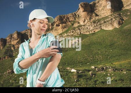 Eine Sportlerin in einer Mütze und nuzhniki schaltet die Songs auf ihr Handy während einer Outdoor-Übung vor dem Hintergrund Stockfoto