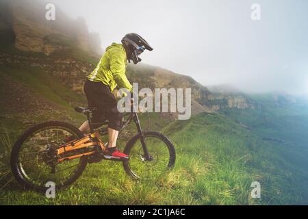 Ein Mann in einem Berghelm mit dem Mountainbike fährt um die schöne Natur bei bewölktem Wetter. Bergab Stockfoto