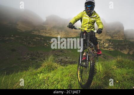 Ein Mann in einem Berghelm mit dem Mountainbike fährt um die schöne Natur bei bewölktem Wetter. Bergab Stockfoto