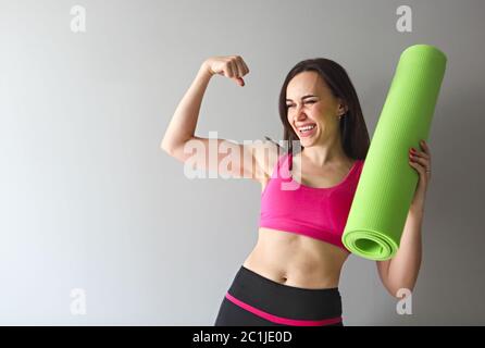 Attraktive Frau trägt rosa Sportbekleidung mit grünen Yoga oder Fitness-Matte nach dem Training zu Hause oder im Club Stockfoto