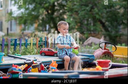 Ein Kind spielt auf dem Spielplatz mit Spielzeug im Sandkasten. Kleinkind Junge spielt im Sommer im Sand. Fröhlicher Kinderurlaub draußen. Stockfoto