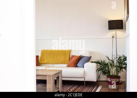 Einfache, industrielle Innenarchitektur des Wohnzimmers mit Holztisch, der vor einem grauen Sofa mit gelber und blauer Polsterung steht Stockfoto
