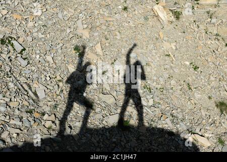 Zwei Schatten von Fotografen auf der Erde, die mit hochgezogene Hände bergauf gehen und um Sieg und Erfolg schreien. Silhouetten von Stockfoto