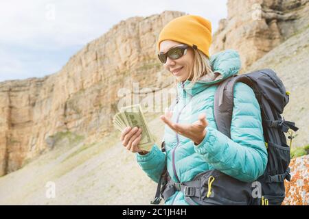 Ein Reisender in einem Hut und Sonnenbrille hält hundert Dollar Scheine in den Händen eines Fans vor dem Hintergrund von Felsen auf dem Nat Stockfoto