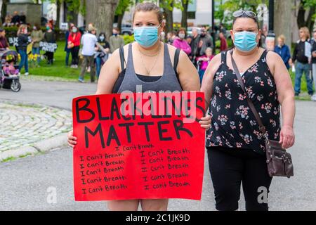 Saint John, NB, Kanada - 14. Juni 2020: Black Lives Matter Rallye. Zwei Frauen tragen Masken, eine trägt ein Protestschild. Stockfoto