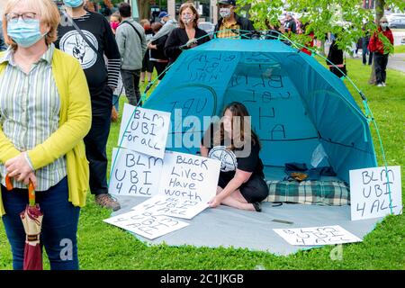 Saint John, NB, Kanada - 14. Juni 2020: Black Lives Matter Rallye. Eine Frau sitzt in einem blauen Zelt, umgeben von Schildern. Stockfoto