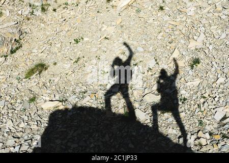 Zwei Schatten von Fotografen auf der Erde, die mit hochgezogene Hände bergauf gehen und um Sieg und Erfolg schreien. Silhouetten von Stockfoto