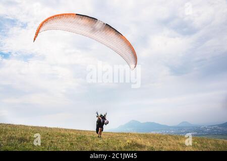 Ein Mann Gleitschirm, der vom Rand des Berges mit Feldern im Hintergrund abheben. Gleitschirmfliegen Stockfoto