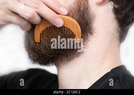 Nahaufnahme eines jungen Mannes styling seinem langen Bart mit einem Kamm, während allein in einem Studio vor einem weißen Hintergrund Stockfoto