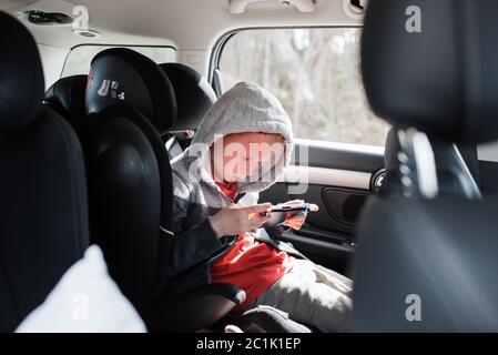 Boy saß auf seinem Autositz und spielte ein Nintendo-Video Spielkonsole Stockfoto