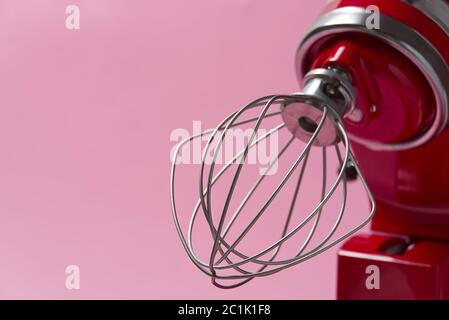 Stilvoller Küchenmixer in Rot mit Trennpfad auf rosa Hintergrund isoliert. Professionelle elektrische Rührmaschine aus Stahl mit Metallbesen Stockfoto