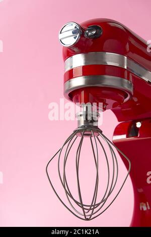 Stilvoller Küchenmixer in Rot mit Trennpfad auf rosa Hintergrund isoliert. Professionelle elektrische Rührmaschine aus Stahl mit Metallbesen Stockfoto