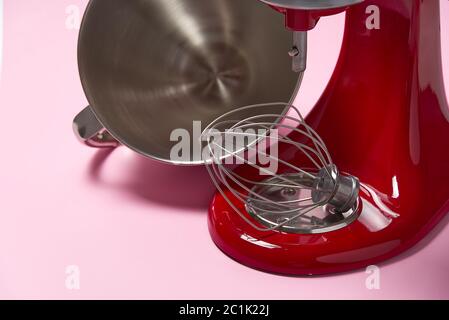 Stilvoller Küchenmixer in Rot mit Trennpfad auf rosa Hintergrund isoliert. Professionelle elektrische Rührmaschine aus Stahl mit Metallbesen Stockfoto
