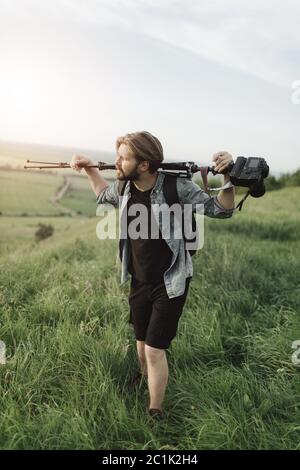 Müde Mann hält Stativ mit Kamera beim Klettern auf Hügel Stockfoto