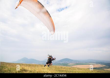 Ein Mann Gleitschirm, der vom Rand des Berges mit Feldern im Hintergrund abheben. Gleitschirmfliegen Stockfoto