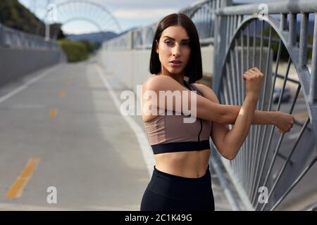 Jogger schaut weg und streckt die Arme auf der Brücke Stockfoto