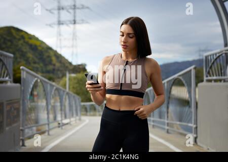 Frau in Sportbekleidung mit Smartphone, während auf der Brücke stehen Stockfoto