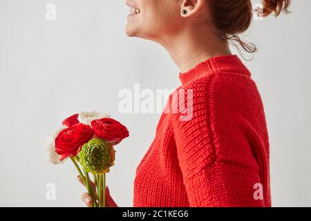 Happy girl in einem roten Strickpullover mit einem schönen Bouquet von bunten Ranunculus Blumen um einen grauen Hintergrund Witz Stockfoto