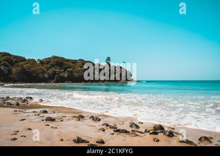 Schöner abgelegener Strand auf einer einsamen Insel. Blaues Wasser und weiße Wellen schwameln an einem Sandstrand mit Steinen in Sri Lanka. Entfliehen Sie auf die abgelegene Insel Stockfoto