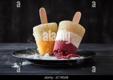 Berry sorbet Lolly auf einem Stick in eine Platte mit Scheiben von Eis auf einem schwarzen Holz- Hintergrund. Diätetische Dessert Stockfoto