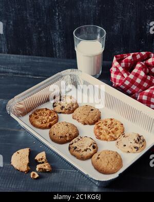 Backblech mit hausgemachten Keksen für Santa mit Erdnüssen, Chocolate Chips, Rosinen und ein Glas mit Milch auf einem dunklen Hintergrund wi Stockfoto