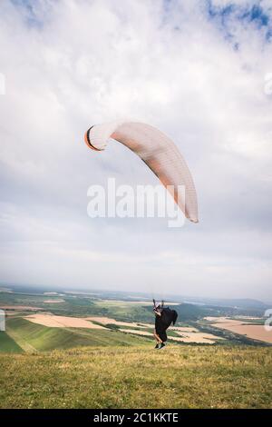 Ein Mann Gleitschirm, der vom Rand des Berges mit Feldern im Hintergrund abheben. Gleitschirmfliegen Stockfoto