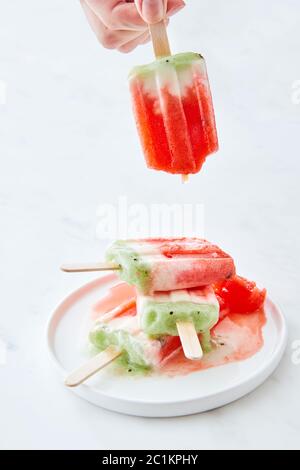 Eis am Stiel in einem Teller mit Spritzern. Hand hält eine Frau eines schmelzenden Eis auf einem weißen Hintergrund mit Kopie Raum Stockfoto