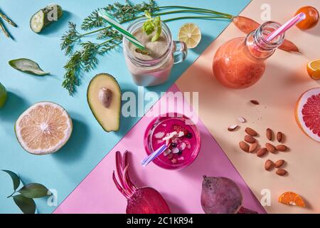 Orange, grüne und rote Smoothies aus buntem Naturgemüse und Obst in einer Glasflasche mit Plastikhalmen auf einer Tricolor Stockfoto