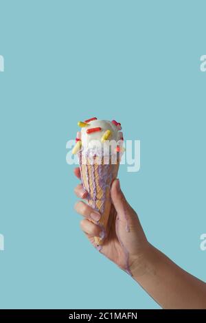 Waffelkegel mit schmelzendem Eis und Tabletten, hält weibliche Hand auf blauem Hintergrund mit Kopierraum. Stockfoto